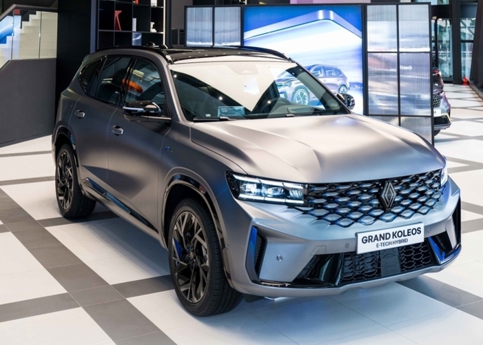 실내 전시장에 진열된 매트 그레이 색상의 르노 브랜드 SUV 차량, 'GRAND KOLEOS E-TECH HYBRID'가 정면 45도 각도로 보이고 있다.