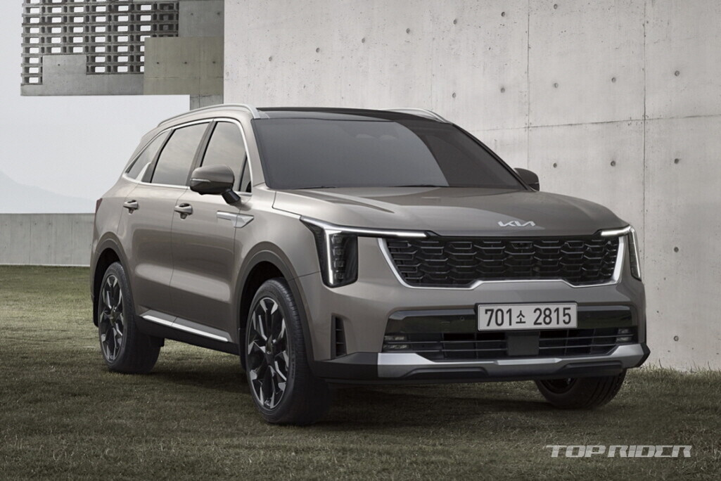 회색 기아 SUV 차량이 잔디 위에 주차되어 있고, 배경에는 콘크리트 벽과 건물이 보인다.